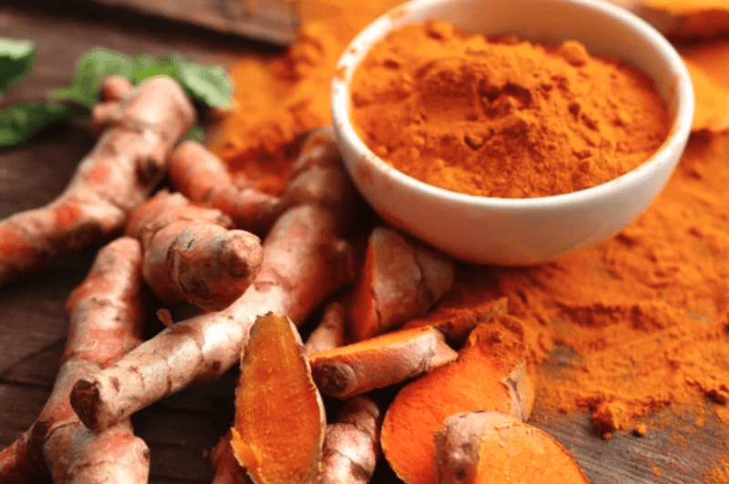 bowl of turmeric next to an array of turmeric root plants