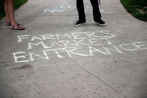 chalkboard sidewalk sign reading "farmers market entrance"