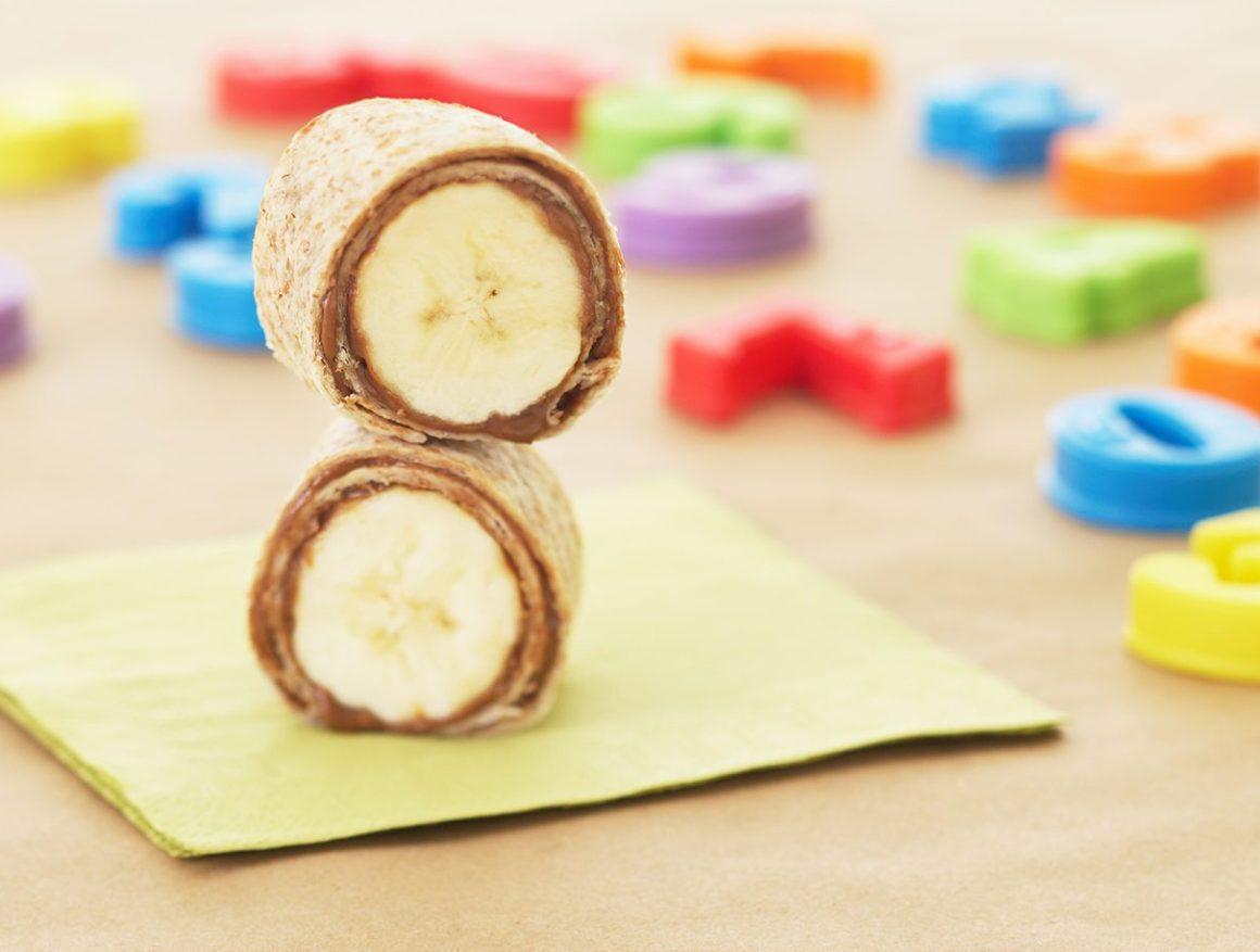 rfrk's banana roll up featuring cocoa chic'pea spread sliced in half on top of yellow napkin and next to colourful letter blocks