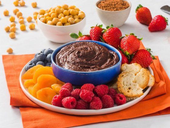 bowl of chocolate hummus, cocoa chic'pea spread, surrounded fruit