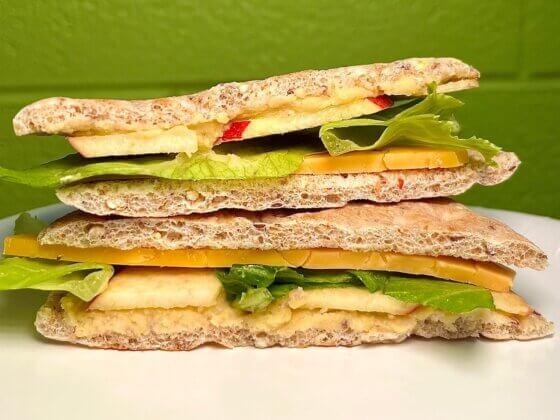 stacked view of hummus & cheddar sandwich with green background on white table