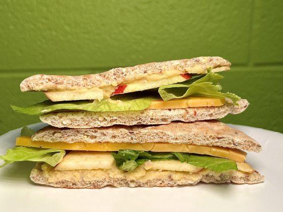 stacked view of hummus & cheddar sandwich with green background on white table