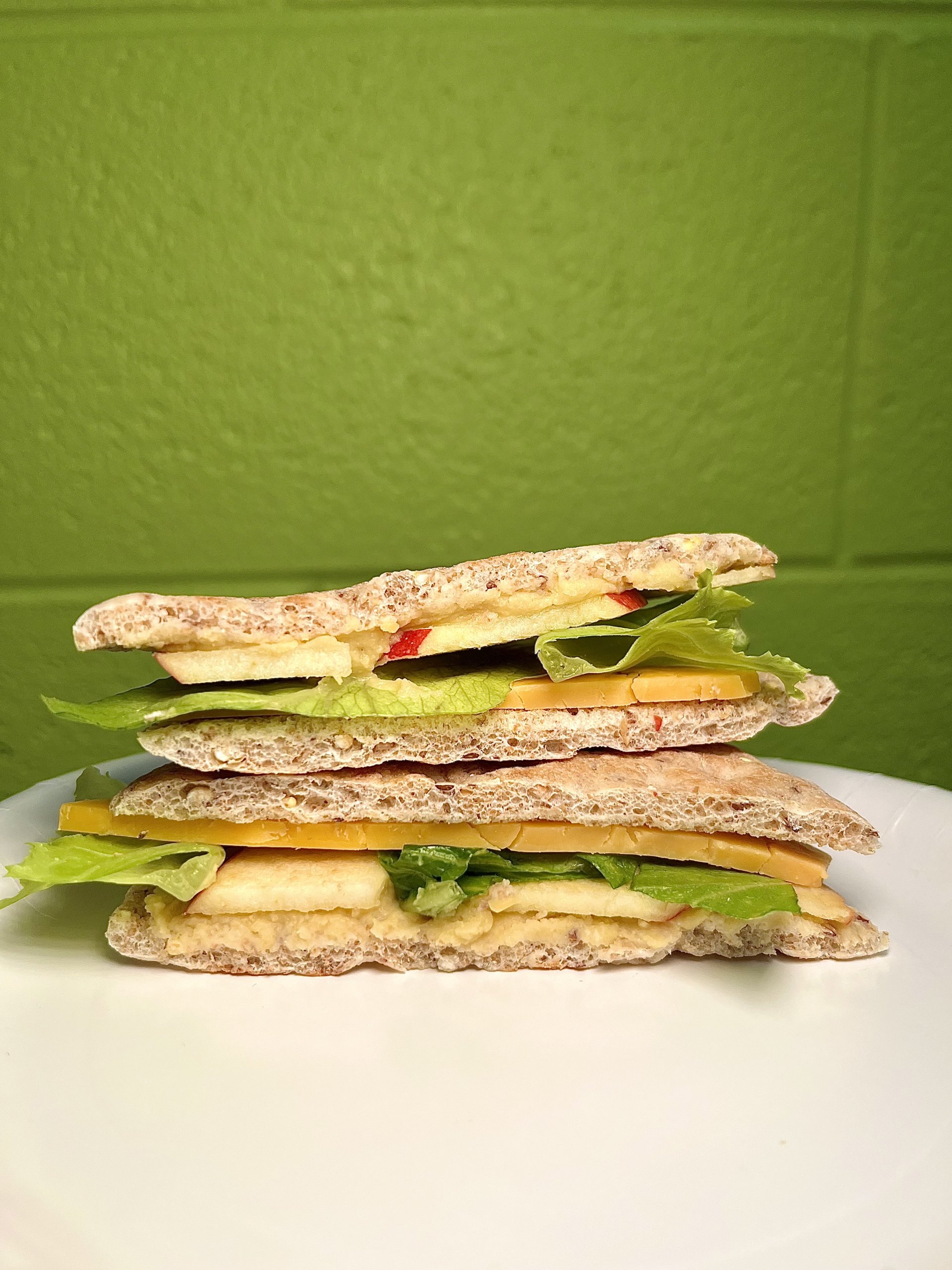 stacked view of hummus & cheddar sandwich with green background on white table