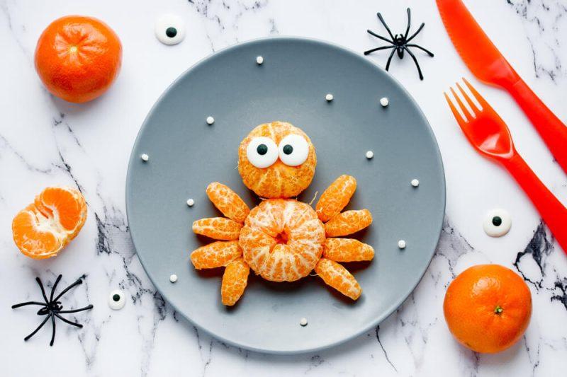 spider snack made with tangerines arranged in the shape of a spider on a gray plate