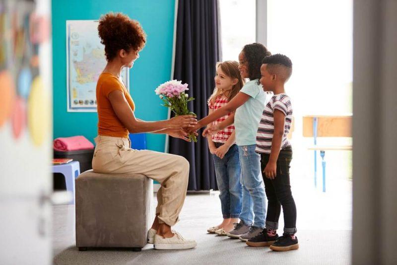 Group Of Elementary School Pupils Giving Female Teacher Thank You Gift Of Flowers