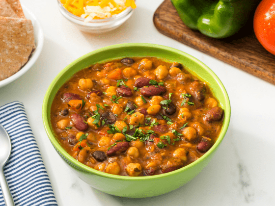 RFRK's chili chili bang bang in a green bowl served on a table next to a spoon and corner view of a tomato and green pepper