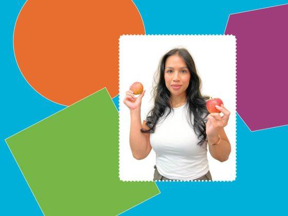 woman with white shirt posing for a meet our team photo, holding two apples in front of colourful background