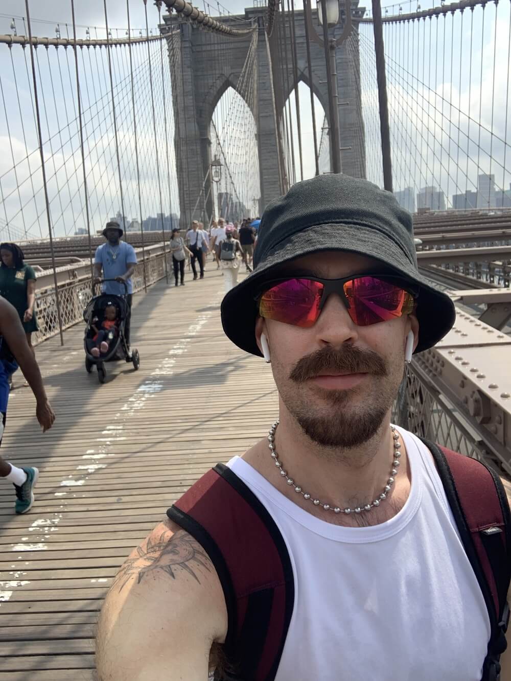 Man with sun hat and glasses and white tank top on brooklyn bridge 