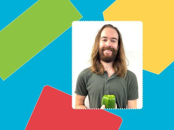 man smiling with long hair and beard with army green shirt holding green pepper in front of white background and colourful border