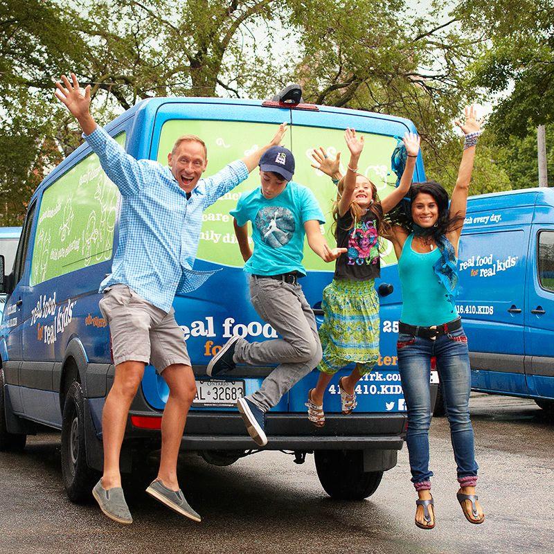 man, boy, girl and woman jumping happily in front of Real Food for Real Kids delivery van