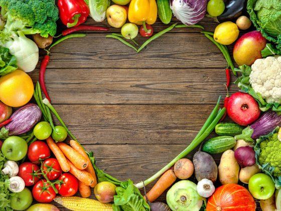 Assortment of fruits and veggies shaped in a heart on top of wooden background