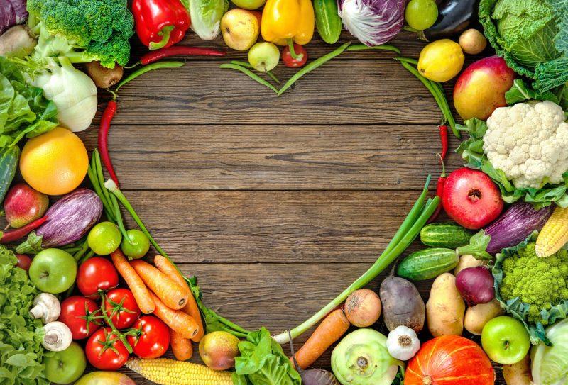 Assortment of fruits and veggies shaped in a heart on top of wooden background