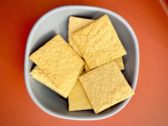 small blue bowl with 8 sourdough crackers on top of orange-red table background