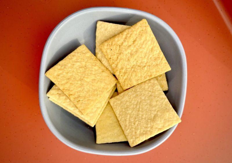 small blue bowl with 8 sourdough crackers on top of orange-red table background