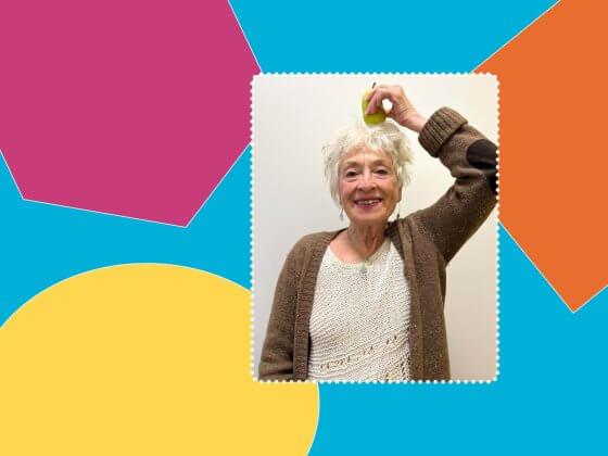 lady with white shirt and brown sweater smiling holding pear on top of head in front of multi colour background of purple, blue, orange and yellow