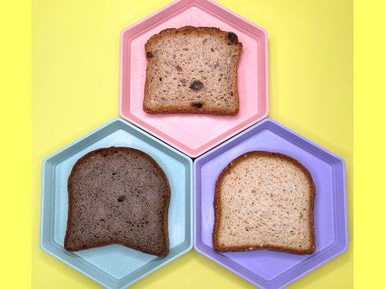 yellow background and three plates, pink, blue and purple with slice of gluten-free bread on each plate