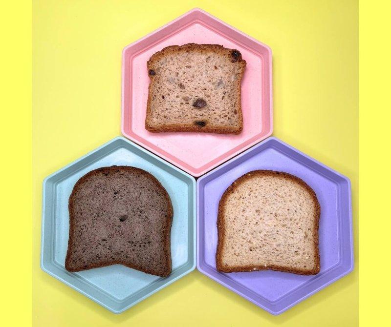 yellow background and three plates, pink, blue and purple with slice of gluten-free bread on each plate