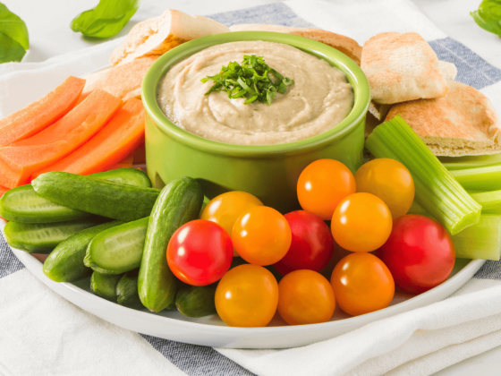 green ramekin filled with rfrk's beany basil dip surrounded by veggies including carrots, baby tomatoes, celery and pita