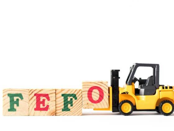 toy truck picking up red and green building blocks that read "FEFO" for first expire, first out with white background
