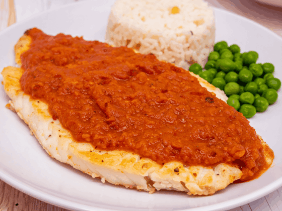 masala fish filet with masala marinade on top next to rice and green peas