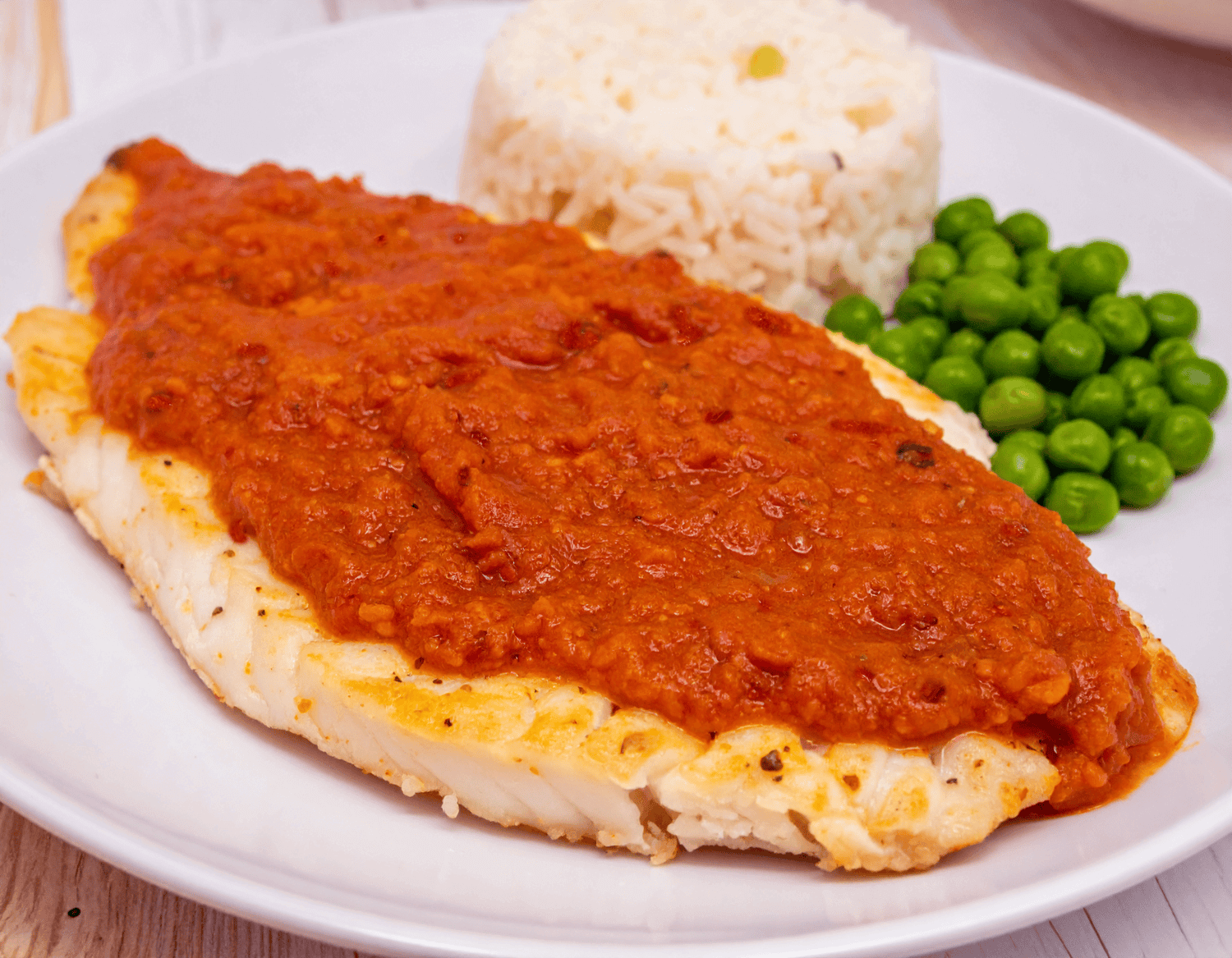 masala fish filet with masala marinade on top next to rice and green peas