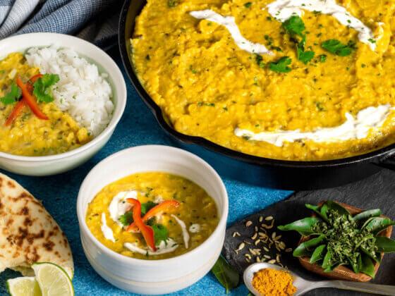 professional photo of RFRK's sunshine dahl recipe in large serving pot with two bowls next to it and accompaniments