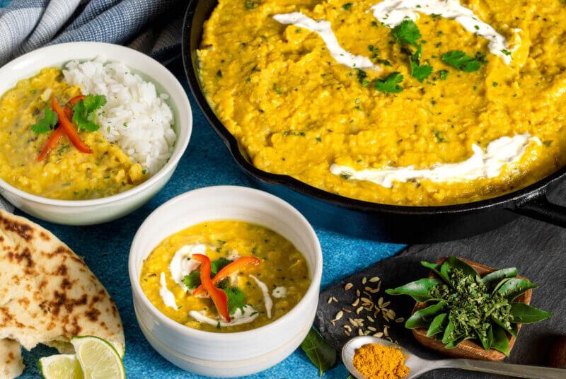 professional photo of RFRK's sunshine dahl recipe in large serving pot with two bowls next to it and accompaniments