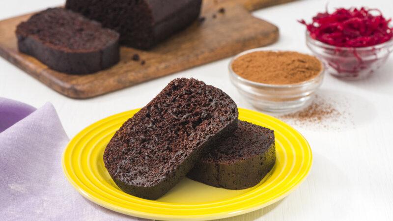 RFRK's cocoa beet loaf one slice on top of the other, served on a yellow plate next to cutting board with rest of the full loaf