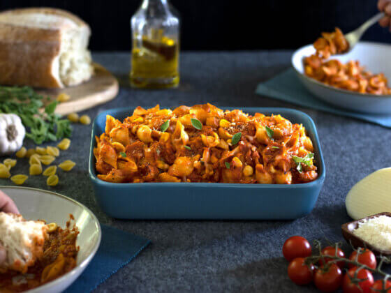 RFRK's vegetarian pasta bake in a large blue casserole style dish with bread, tomatoes, olive oil, cheese scattered around main casserole dish