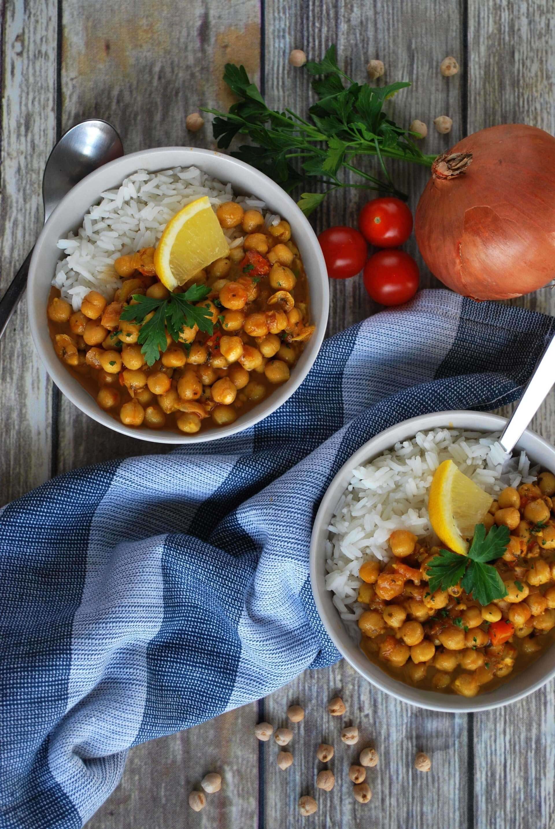 two bowls of rfrk chickpea chowder topped with cilantro and lemon wedge served over rice