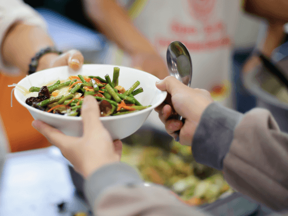 volunteer hands a bowl of veggies to someone