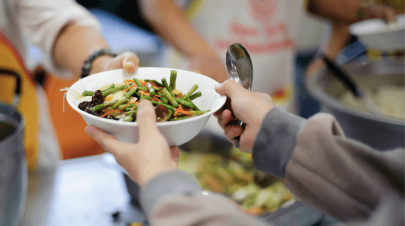 volunteer hands a bowl of veggies to someone