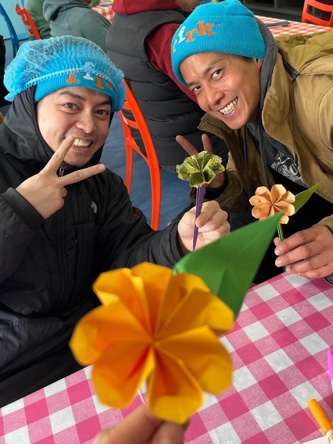 flower origami with two rfrk staff smiling holding up a peace sign wearing blue toques