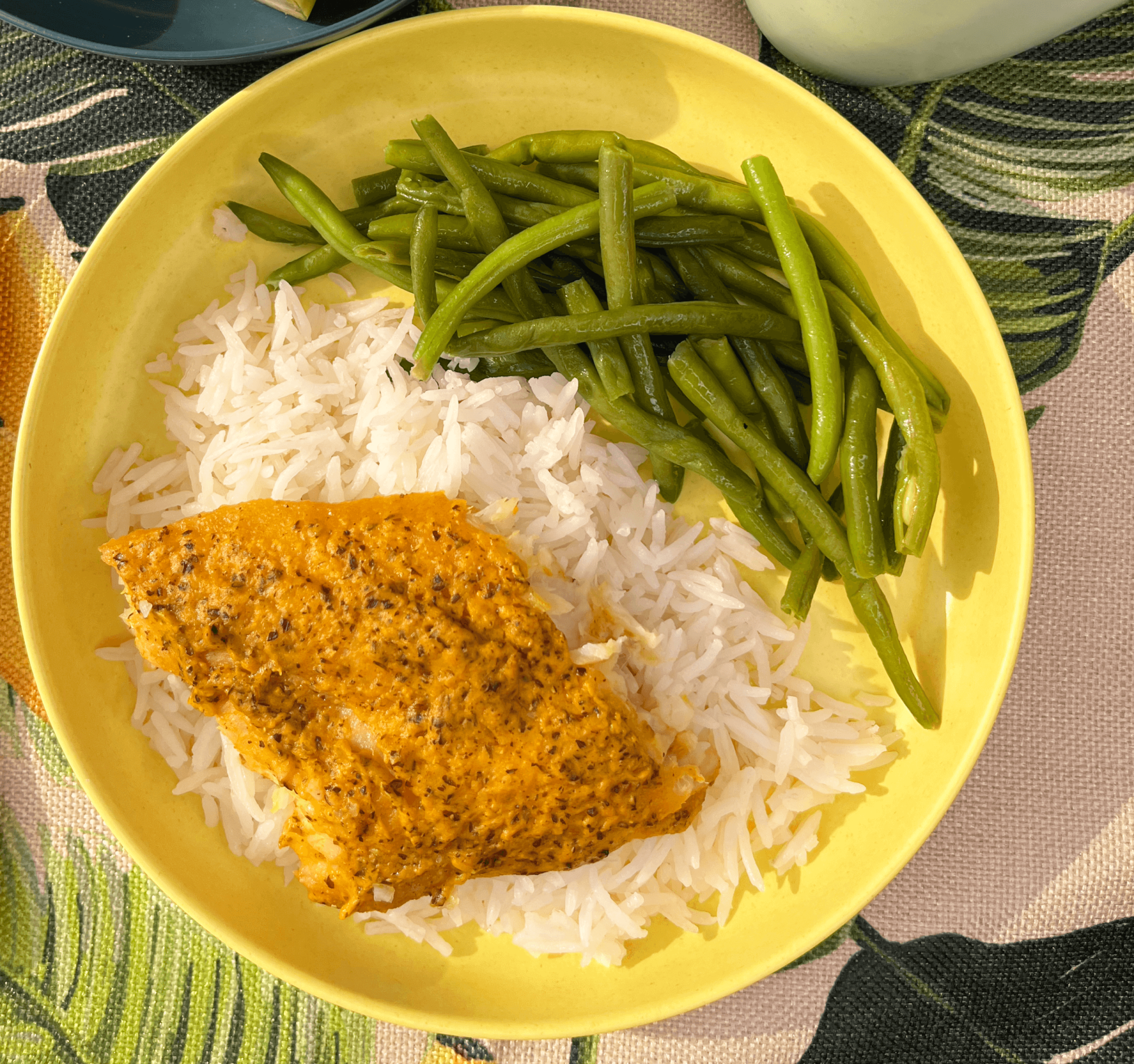 carrot and flax fish served on top of basmati rice with green beans on a yellow plate and tropical themed placemat