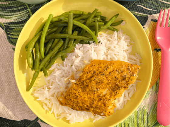 carrot and flax fish served on top of basmati rice with green beans on a yellow plate and tropical themed placemat