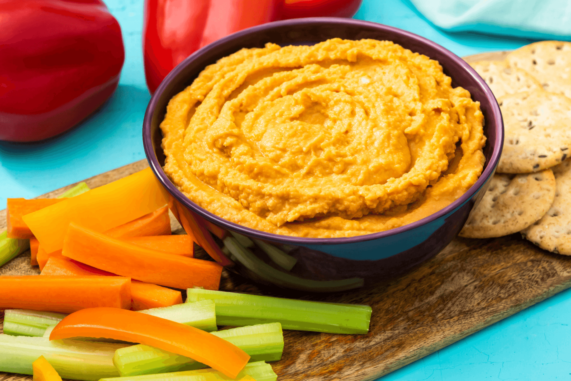 rfrk's red pepper hummus in small black bowl next to veggie sticks, carrot sticks and crackers
