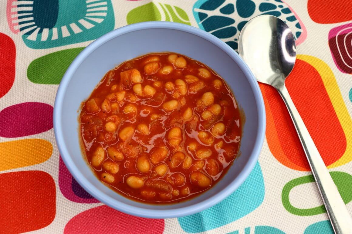rfrk's slow cooked beans with spoon in small pale blue bowl on top of placement with colourful shapes. served to vegetarians who can't have chickpeas