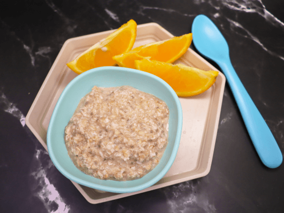 cinnamon and chia oatmeal in small blue bowl next to blue spoon on beige plate next to sliced oranges
