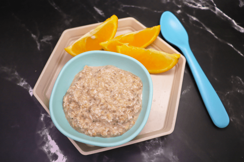 cinnamon and chia oatmeal in small blue bowl next to blue spoon on beige plate next to sliced oranges