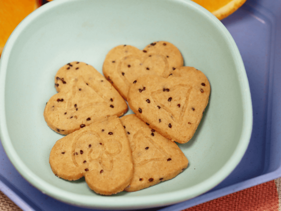 five heart shaped coconut & chia cookies in small light blue bowl next to orange slices in the background