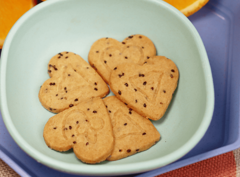 five heart shaped coconut & chia cookies in small light blue bowl next to orange slices in the background