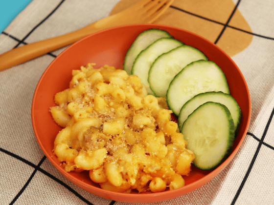 bowl of skipjack tuna mac'n cheese next to sliced cucumber in orange bowl next to fork