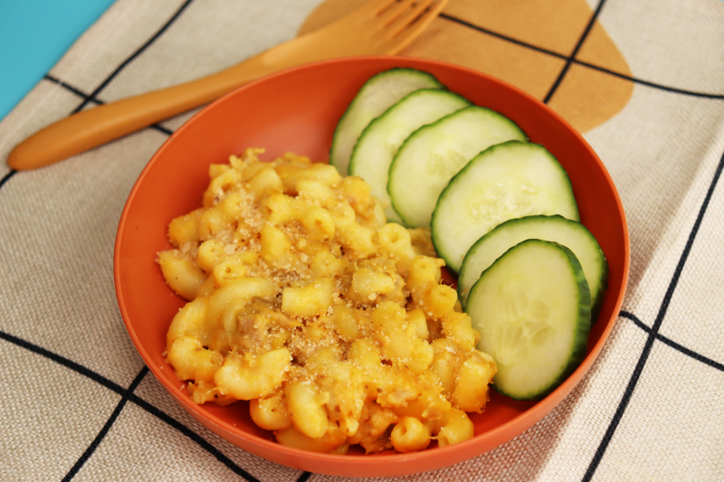 bowl of skipjack tuna mac'n cheese next to sliced cucumber in orange bowl next to fork