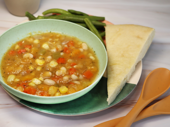 bowl of three sisters soup with beans, squash and corn served in light green bowl next to bread and green beans