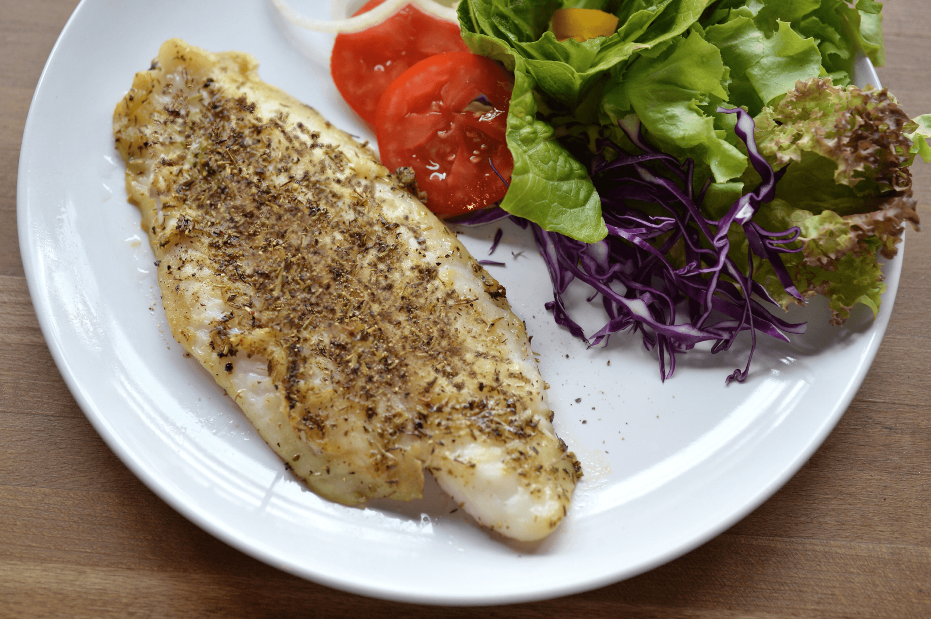 basa fish filet topped with marinade served on plate with fork, lemon and side assorted veggies
