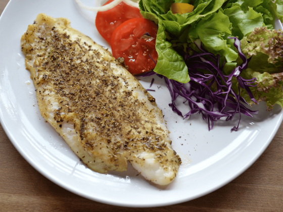 basa fish filet topped with marinade served on plate with fork, lemon and side assorted veggies