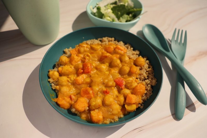 bowl of vegetarian dish pumpkin chana curry in a teal bowl next to teal kids cutlery